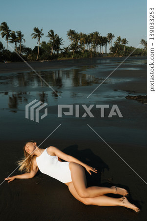 Woman lays on the beach at sunset near palm trees Woman lays on the beach at sunset near palm trees 139033253