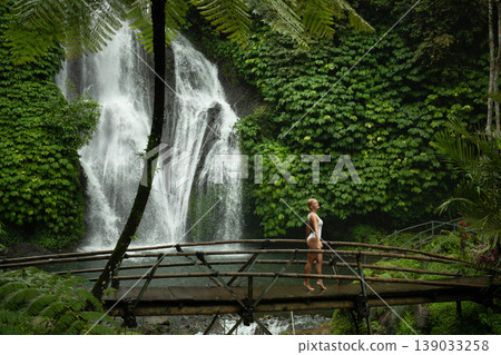 Person walks on a bridge near a waterfall and lush plants Person walks on a bridge near a waterfall and lush plants 139033258