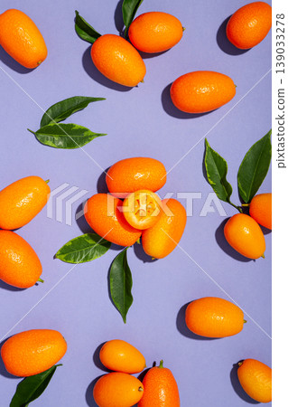 Kumquats are arranged with green leaves on a purple surface Kumquats are arranged with green leaves on a purple surface 139033278