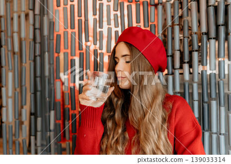 Woman Beret Water drinking from a glass in a cafe while wearing a red sweater for healthy hydration 139033314