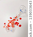 A broken Erlenmeyer flask and other lab equipment are shown with a red liquid spilled across a white background 139033643