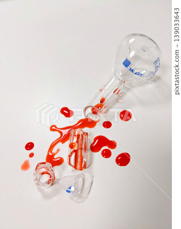 A broken Erlenmeyer flask and other lab equipment are shown with a red liquid spilled across a white background A broken Erlenmeyer flask and other lab equipment are shown with a red liquid spilled across a white background 139033643