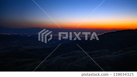 Nightfall over cityscape from elevated hillside with glowing lights 139034325