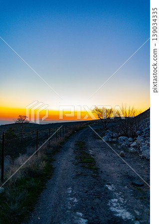 Sunset illuminates dirt trail through rocky, dry hills 139034335