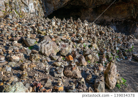 Cave mouth surrounded by rocky slope with sparse vegetation 139034378