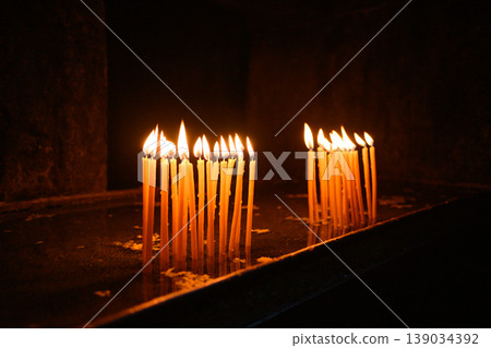 Lit candles in dark church interior, prayer and spirituality concept Lit candles in dark church interior, prayer and spirituality concept 139034392