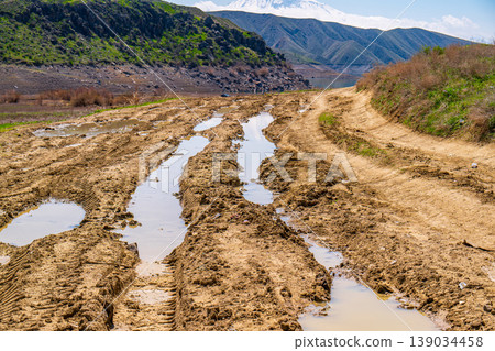 Earthly mud tracks with pooled water lead into mountainous terrain Earthly mud tracks with pooled water lead into mountainous terrain 139034458