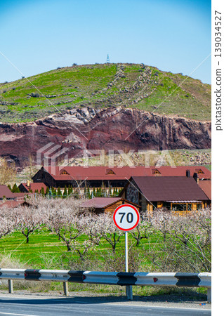 Speed limit 70 sign near blooming orchard and wooden house Speed limit 70 sign near blooming orchard and wooden house 139034527