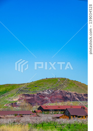Cabin village nestled at foot of grassy hill with exposed rock Cabin village nestled at foot of grassy hill with exposed rock 139034528