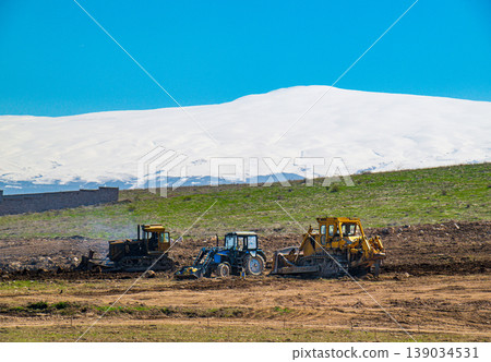 Tractors working in field with snowy mountain backdrop Tractors working in field with snowy mountain backdrop 139034531