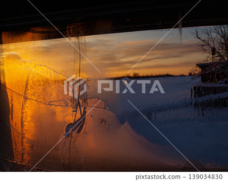 Red-orange sunset ray of the northern sun through a small window. Steam on cold glass creates a dramatic contrast between winter frost and warm light. Atmospheric ray in a moody interior. Red-orange sunset ray of the northern sun through a small window. Steam on cold glass creates a dramatic contrast between winter frost and warm light. Atmospheric ray in a moody interior. 139034830