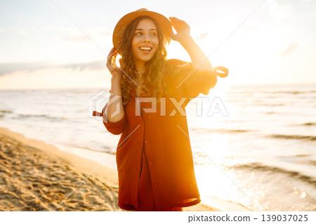 Carefree woman tourist walking along ocean sandy beach at sunset. Travel, weekend, lifestyle concept Carefree woman tourist walking along ocean sandy beach at sunset. Travel, weekend, lifestyle concept 139037025