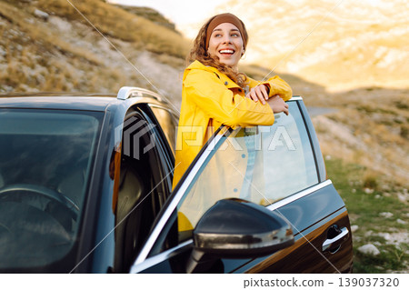 A cheerful traveler enjoying a scenic mountain view while sitting on the trunk. Travelling by car. A cheerful traveler enjoying a scenic mountain view while sitting on the trunk. Travelling by car. 139037320