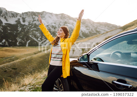 A cheerful traveler enjoying a scenic mountain view while sitting on the trunk. Travelling by car. 139037322