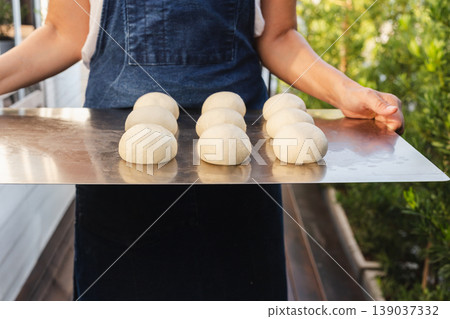 Baker holding a metal tray with fresh raw dough balls prepared for baking. Baker holding a metal tray with fresh raw dough balls prepared for baking. 139037332