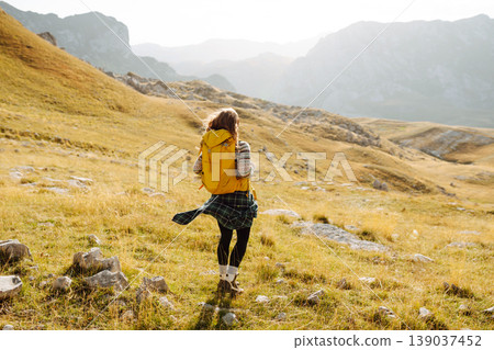 Traveler woman with a bright yellow backpack strolls through golden meadows. Active lifestyle Traveler woman with a bright yellow backpack strolls through golden meadows. Active lifestyle 139037452