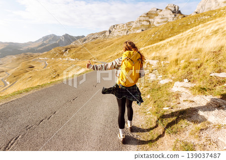 Hitchhiking woman traveler try to stop car on the mountain road. Travel and vacation theme Hitchhiking woman traveler try to stop car on the mountain road. Travel and vacation theme 139037487