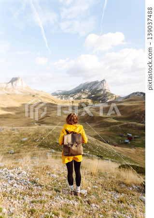 Traveler woman in yellow jacket enjoys hiking on sun. Hiking in mountains with backpacks. Adventure. 139037488