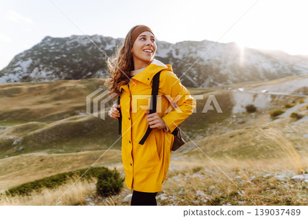 Traveler woman in yellow jacket enjoys hiking on sun. Hiking in mountains with backpacks. Adventure. Traveler woman in yellow jacket enjoys hiking on sun. Hiking in mountains with backpacks. Adventure. 139037489