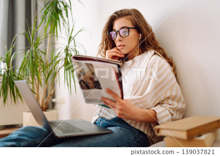 Young woman studying at home with modern laptop, books. Relaxes in the living room. Relax concept. Young woman studying at home with modern laptop, books. Relaxes in the living room. Relax concept. 139037821