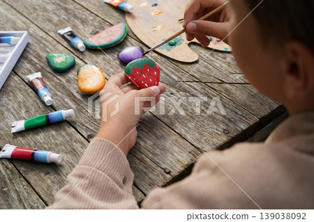Boy paints strawberries on stones, carrots on pebbles making the most adorable stone fruit and veggie collection ever. 139038092