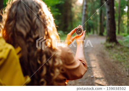 A hiker with curly hair holds a compass in their hands, carefully navigating through a sunlit forest A hiker with curly hair holds a compass in their hands, carefully navigating through a sunlit forest 139038502