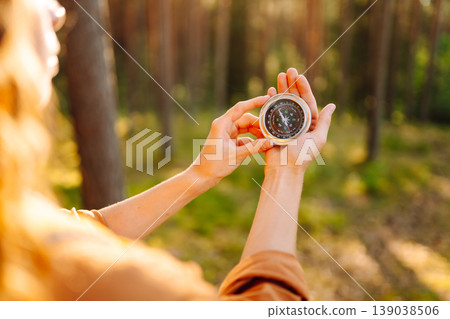 A hiker with curly hair holds a compass in their hands, carefully navigating through a sunlit forest A hiker with curly hair holds a compass in their hands, carefully navigating through a sunlit forest 139038506
