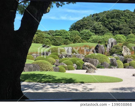 A garden that looks like a picture frame, a beautiful Japanese landscape with white sand and trimmed hedges seen through large trees. A garden that looks like a picture frame, a beautiful Japanese landscape with white sand and trimmed hedges seen through large trees. 139038868