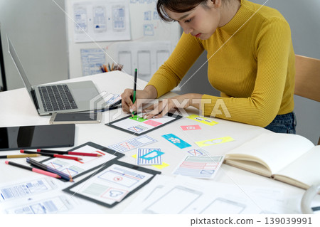 Asian young adult woman designer creating user interface experience prototypes with sketch mockups at home office for new mobile application development Asian young adult woman designer creating user interface experience prototypes with sketch mockups at home office for new mobile application development 139039991