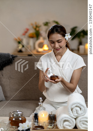 Asian adult woman prepares natural spa essential oil for calming aromatherapy massage at home creating relaxing self care moment 139040147