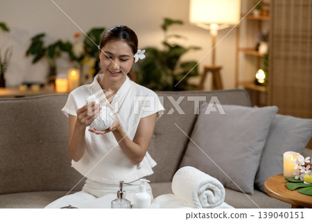 Asian adult woman holds traditional herbal compress preparing relaxing spa therapy at home for wellness and self care ritual 139040151