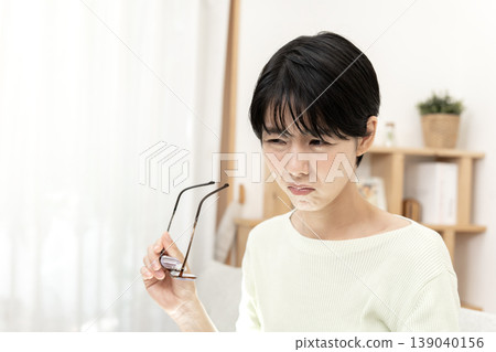 一位日本女性休息時，因眼睛疲勞而按壓眼角，並摘下了眼鏡。 139040156