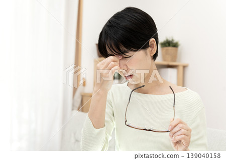 A Japanese woman rests, pressing the corners of her eyes due to eye strain, and taking off her glasses. A Japanese woman rests, pressing the corners of her eyes due to eye strain, and taking off her glasses. 139040158
