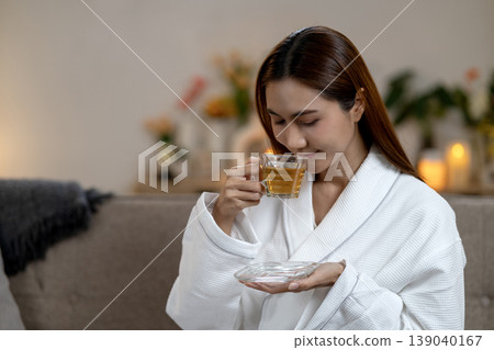 Adult Asian woman enjoying warm herbal tea in white bathrobe at home spa setting for serene self care and relaxation moment Adult Asian woman enjoying warm herbal tea in white bathrobe at home spa setting for serene self care and relaxation moment 139040167