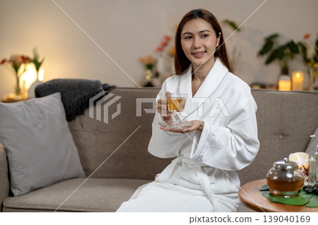 Asian adult woman enjoying herbal tea at home spa wearing a white bathrobe promoting wellness self care and peaceful morning relaxation Asian adult woman enjoying herbal tea at home spa wearing a white bathrobe promoting wellness self care and peaceful morning relaxation 139040169