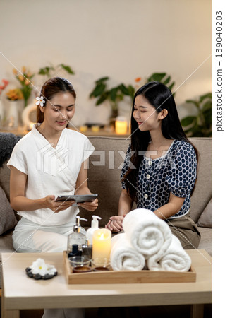 Asian spa therapist discusses wellness plan with client using digital tablet in relaxing modern salon environment Asian spa therapist discusses wellness plan with client using digital tablet in relaxing modern salon environment 139040203