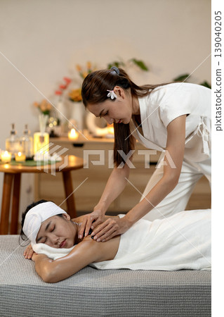 Asian therapist performs hot stone massage on client back for deep relaxation holistic wellness treatment professional spa environment serene atmosphere self care body therapy 139040205