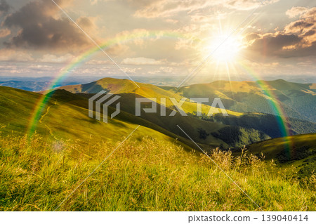 sunset over mountain landscape with alpine meadow in dappled light. carpathian mountain scenery in summer. view in to the distant valley landscape. rolling hills and grassy meadow under the rainbow sunset over mountain landscape with alpine meadow in dappled light. carpathian mountain scenery in summer. view in to the distant valley landscape. rolling hills and grassy meadow under the rainbow 139040414