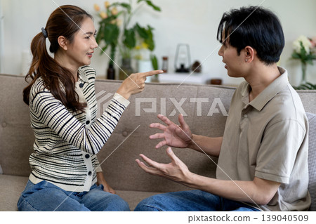 Asian young adult couple engaging heated discussion argument communication disagreement problems relationship issues home sofa living room environment 139040509