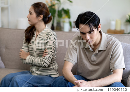 Asian adult couple silently facing disagreement home living room relationship issues domestic conflict emotional distance partners sad unhappy expression Asian adult couple silently facing disagreement home living room relationship issues domestic conflict emotional distance partners sad unhappy expression 139040510