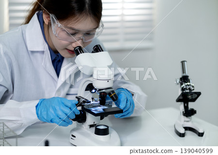 Asian adult woman scientist performs diligent research using microscope in modern laboratory for medical and biological discovery 139040599