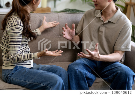 Adult Asian man woman sitting couch discussing problems communication relationship serious conversation home living room solution dialogue gesture hands talking negotiation 139040612