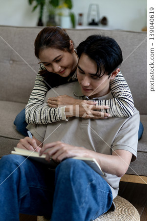 Asian couple young adults collaborate home studying writing notes supporting partner domestic lifestyle education concept 139040619