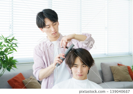 A young Japanese hairdresser curling hair with a curling iron. A young Japanese hairdresser curling hair with a curling iron. 139040687