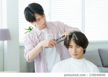 A young Japanese hairdresser curling hair with a curling iron. A young Japanese hairdresser curling hair with a curling iron. 139040690