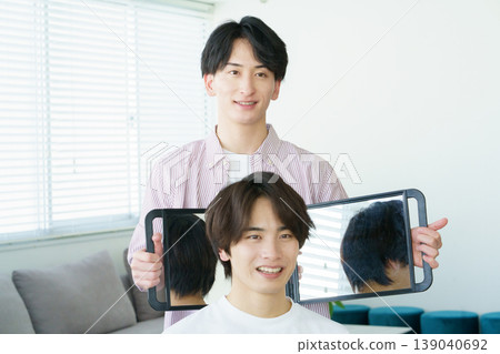 一位年輕的日本髮型師對著鏡子展示他剪的髮型。 139040692