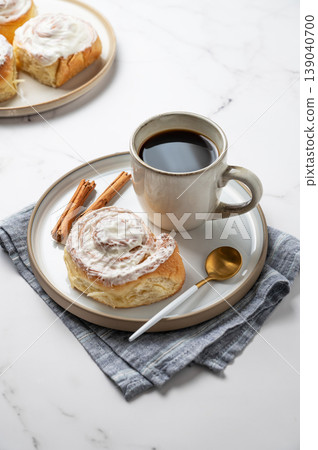 Freshly baked cinnamon rolls with white icing and a cup of black coffee on a light marble background 139040700