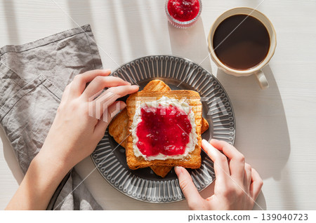 Hand holding toast with sweet berry-fruit jam and cream cheese on a plate on white wooden background 139040723