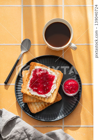 Toast with sweet berry-fruit jam and cream cheese on a dark plate on a yellow tile background Toast with sweet berry-fruit jam and cream cheese on a dark plate on a yellow tile background 139040724