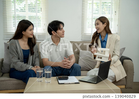 Asian adult real estate agent advises young couple home buying property investment planning future finance discuss mortgage options in modern living room setting Asian adult real estate agent advises young couple home buying property investment planning future finance discuss mortgage options in modern living room setting 139040829